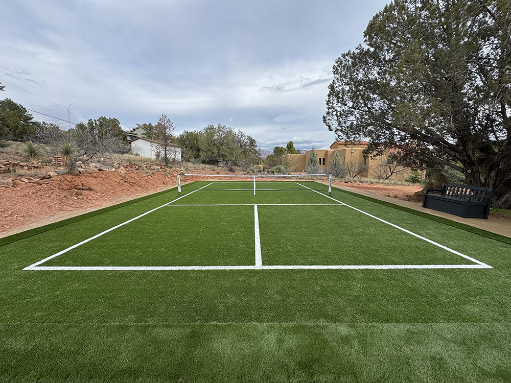 Synthetic grass installation creating a pristine backyard pickleball court with bright white court lines, surrounded by natural red rock landscape and mature trees in Sedona, Arizona.